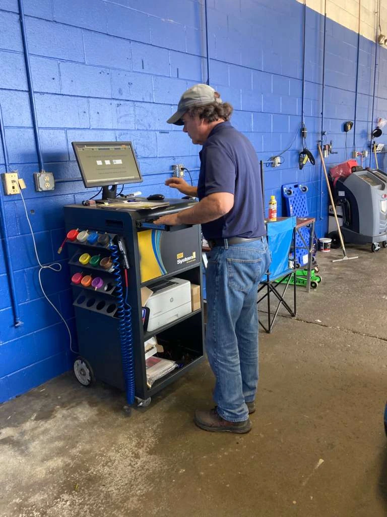 Professional technician using a computerized diagnostic system at an auto repair shop to perform a full auto health check.