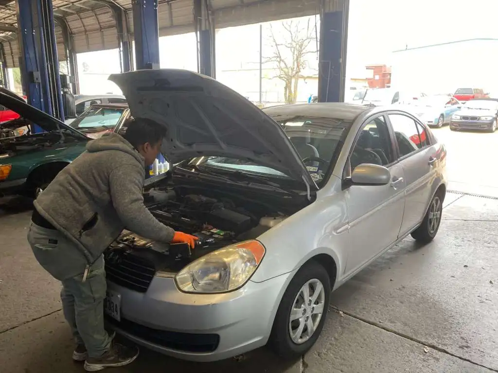 Professional mechanic examining a silver Hyundai car's engine at an auto shop.
