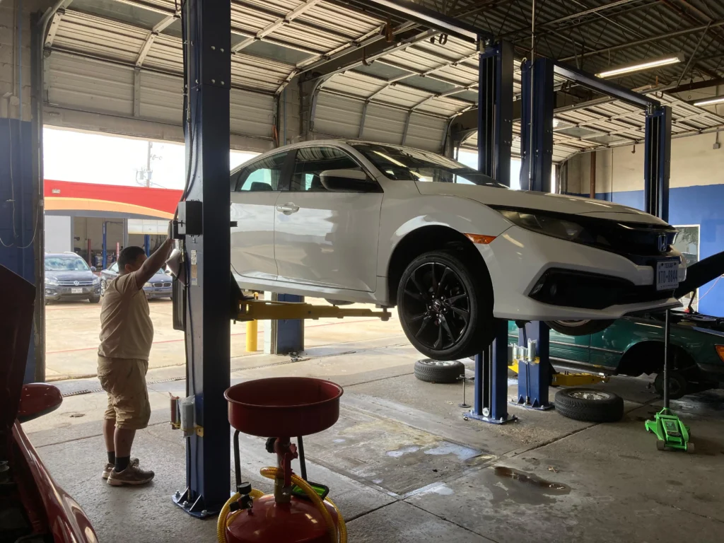 White sedan on a hydraulic lift inside a professional auto repair shop.
