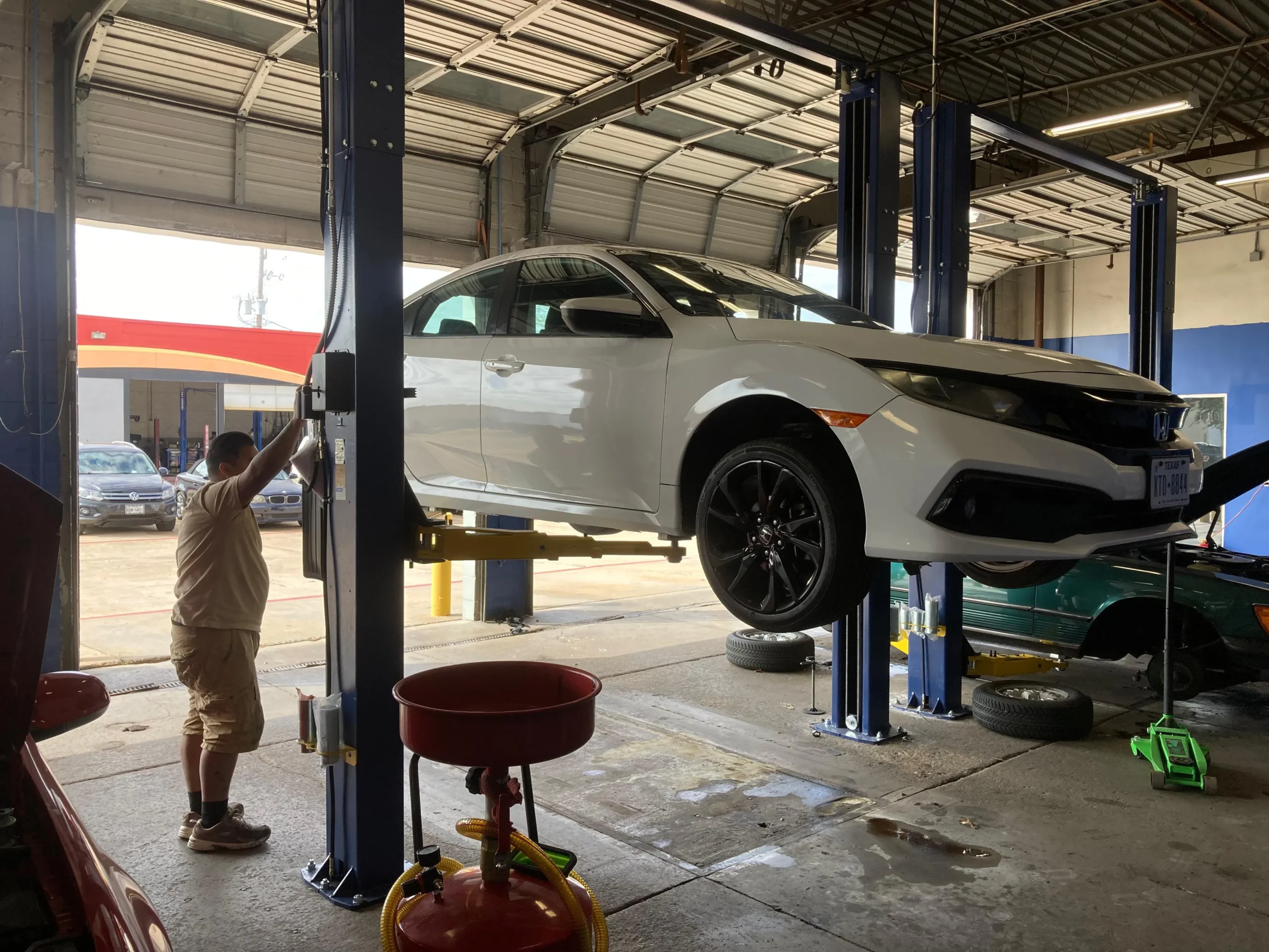 White sedan on a hydraulic lift inside a professional auto repair shop.