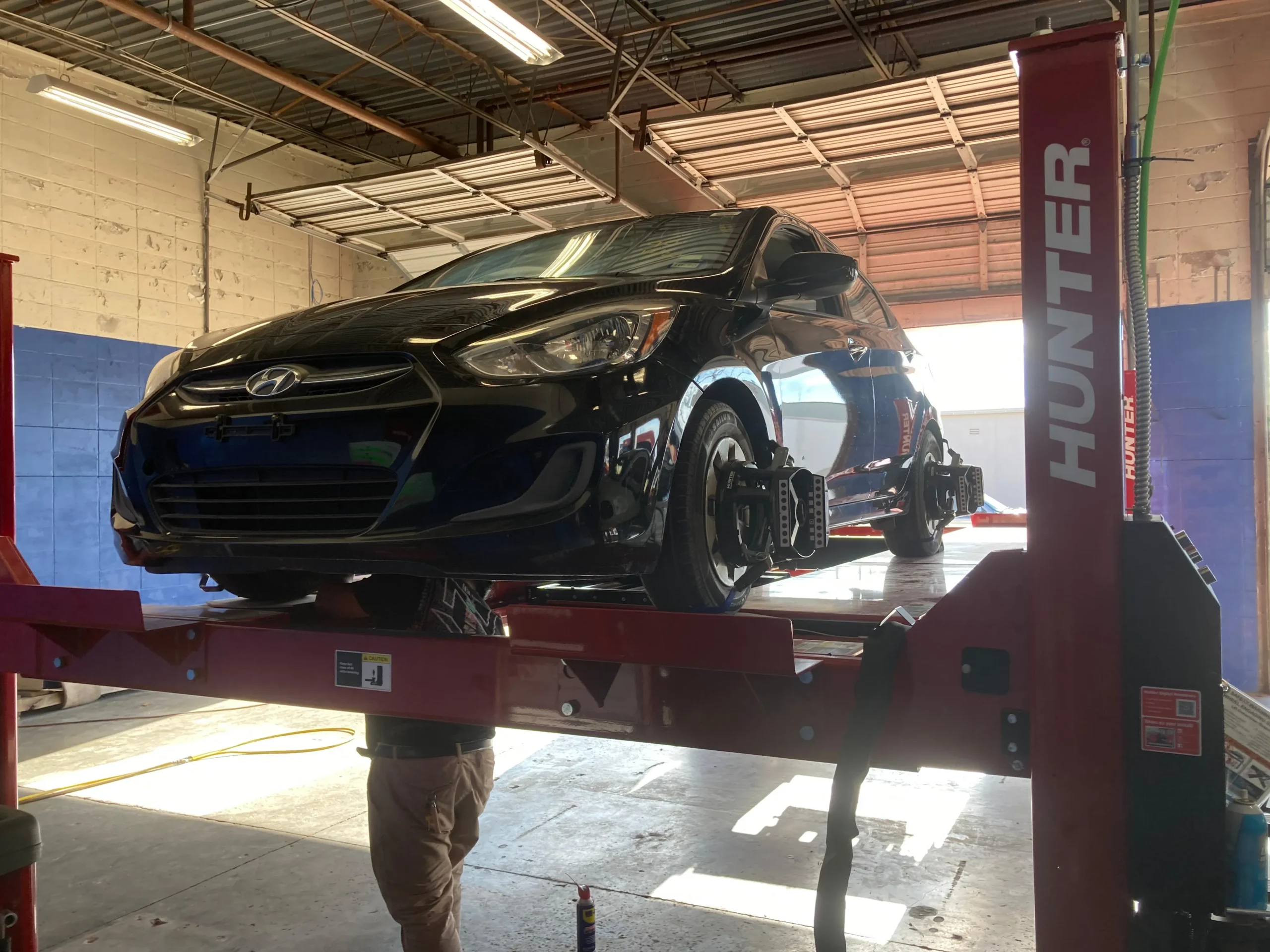 Black Hyundai on a red lift receiving a wheel alignment in a garage.