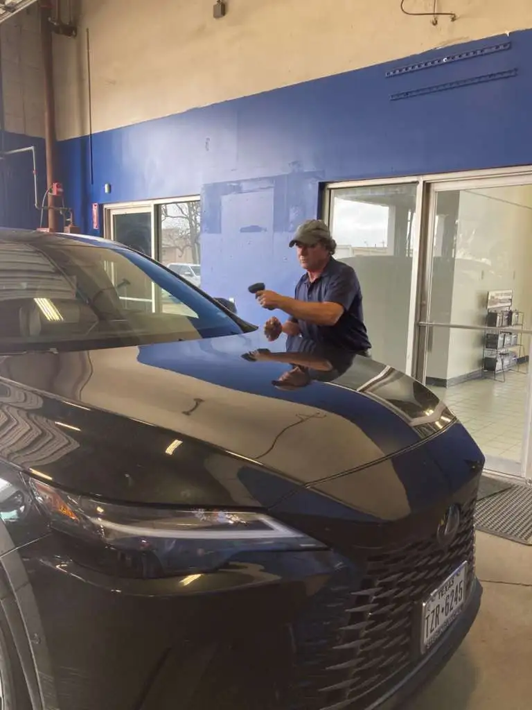 Professional technician performing paint correction or detailing on a black auto at an auto repair shop in Houston TX.