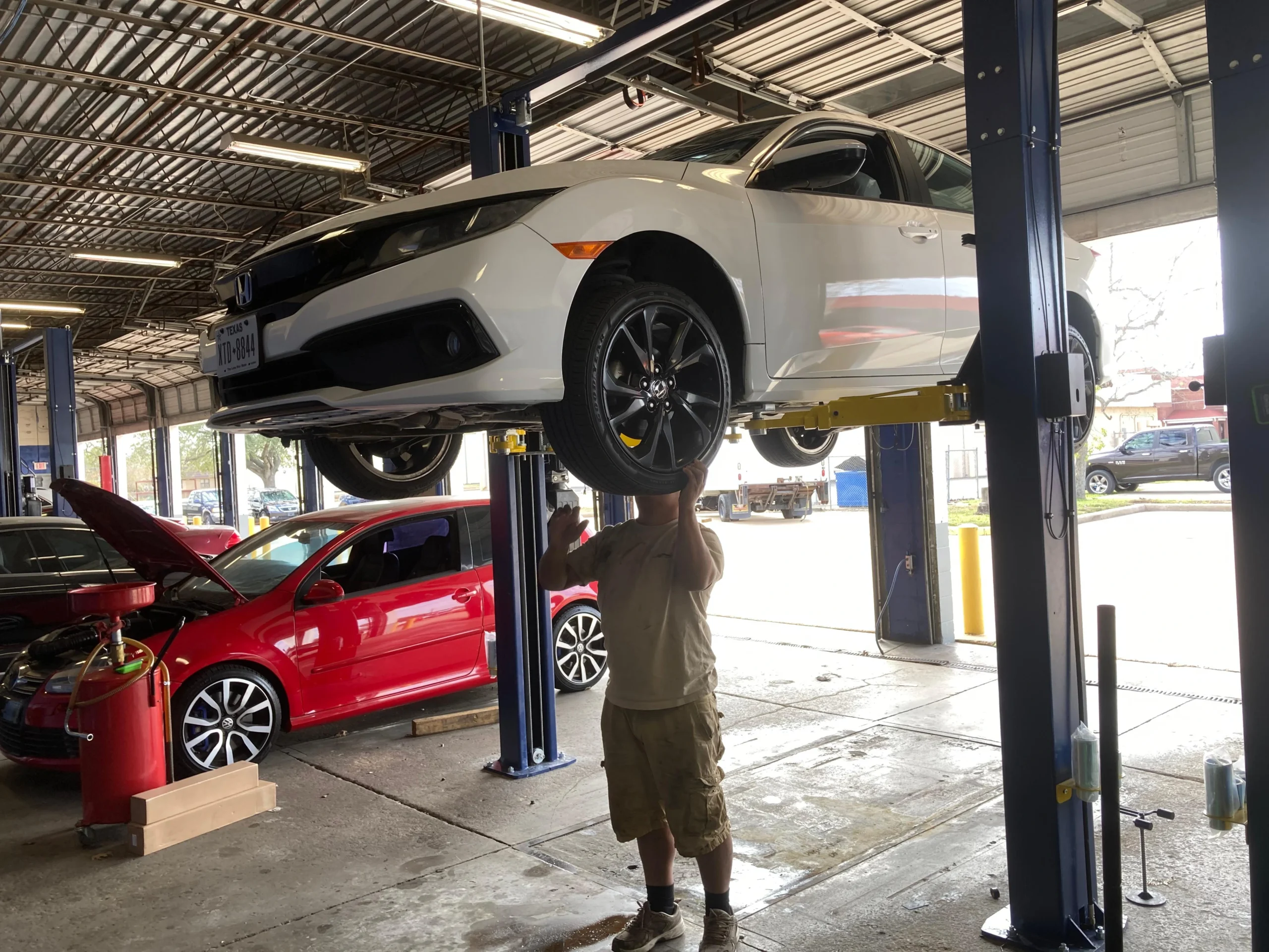 Professional mechanic inspecting a white car on a hydraulic lift at an auto repair shop.