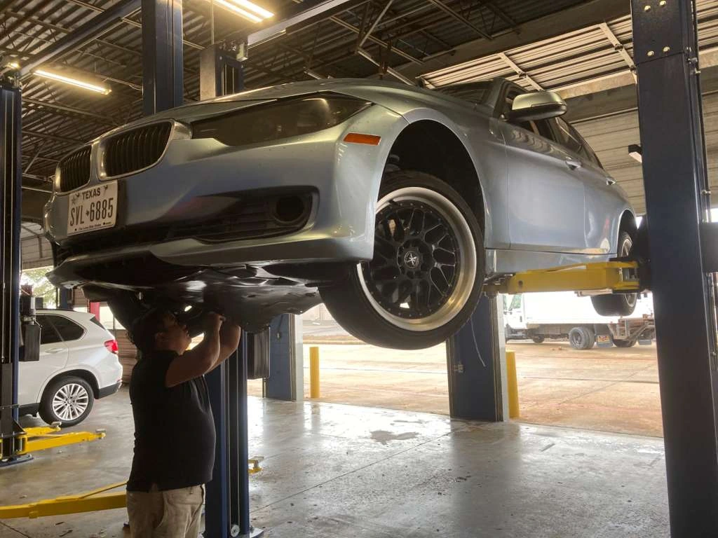 Professional mechanic performing under-auto maintenance on a car at an auto repair shop.