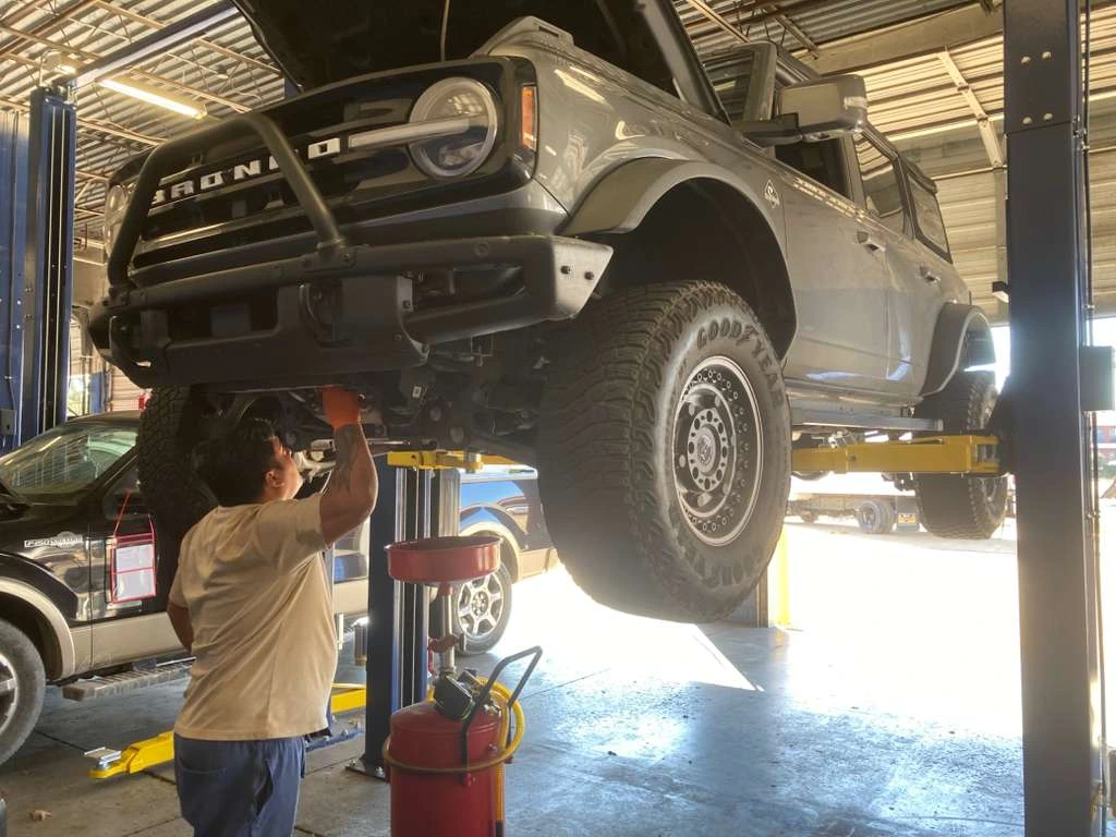 Professional mechanic performing underbody maintenance on a Ford Bronco at an auto repair shop.
