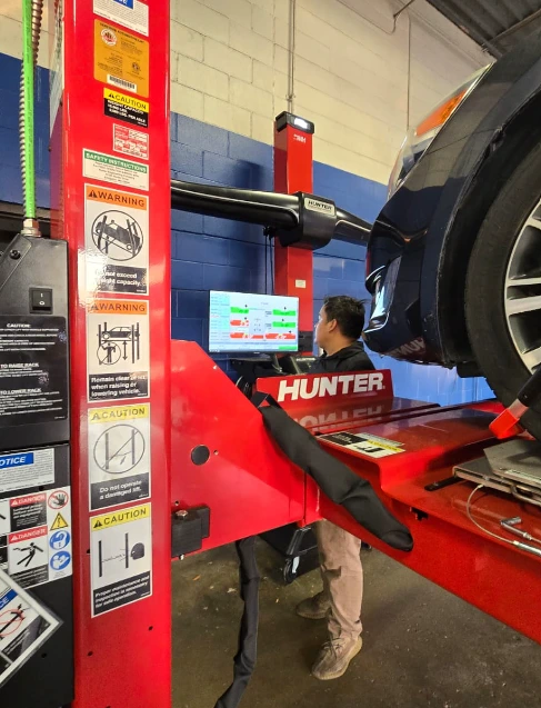 Professional technician performing precision wheel alignment using Hunter Engineering equipment at an auto repair shop.