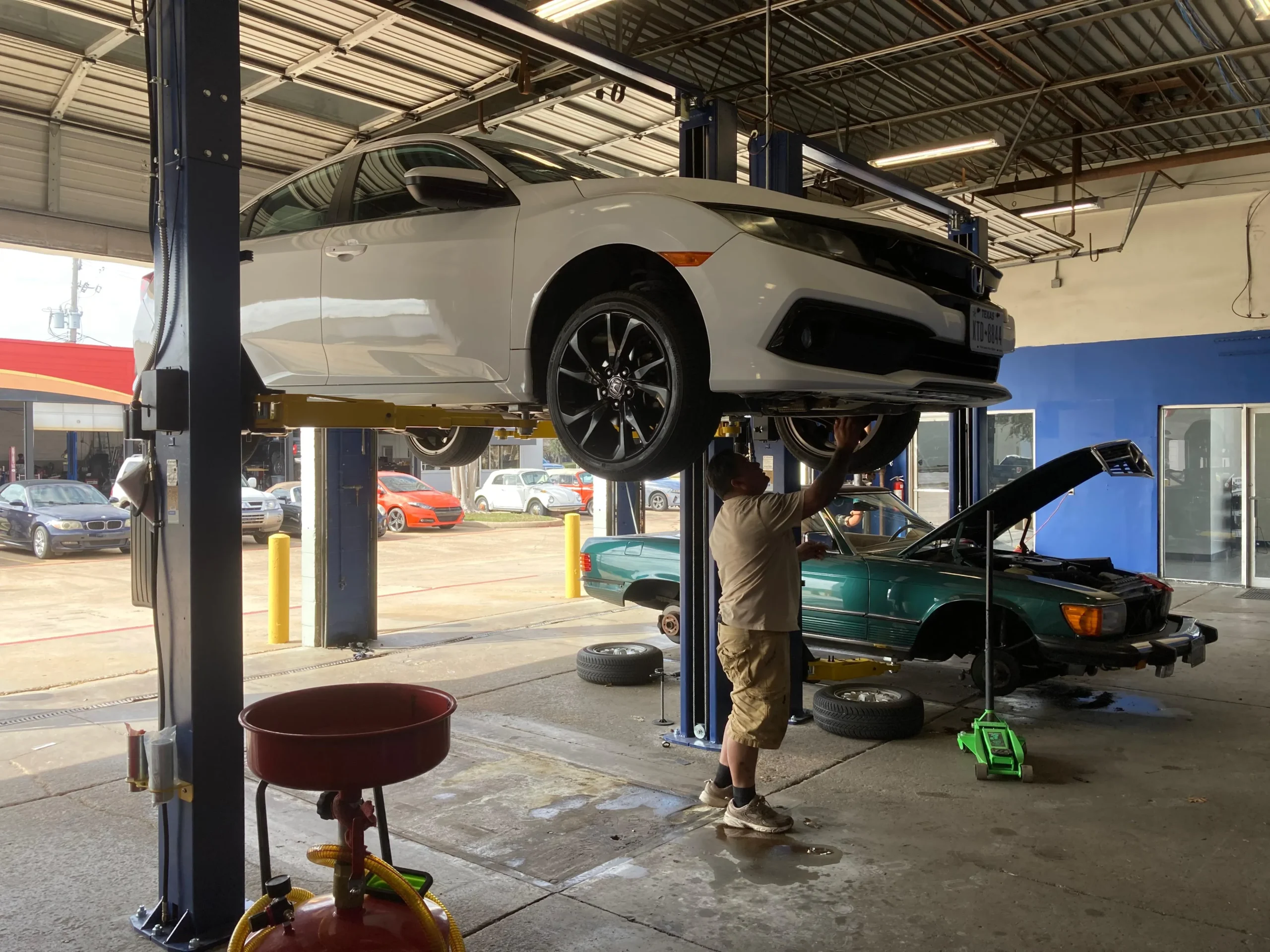 White sedan on a hydraulic lift being inspected by a technician at a professional auto repair shop.