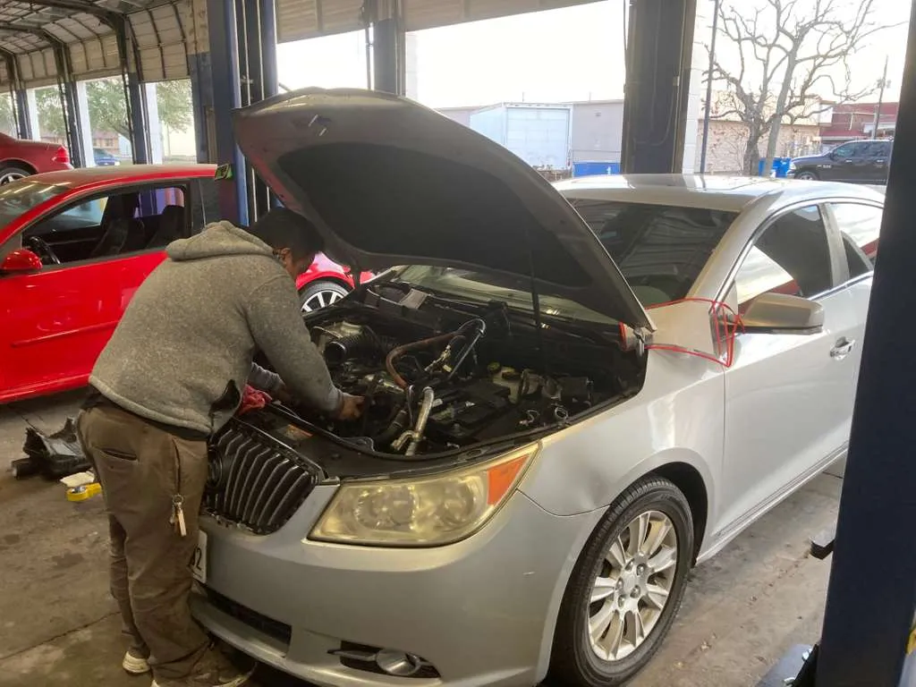 Experienced mechanic performing engine diagnostics and repair on a silver sedan at a professional auto repair shop.