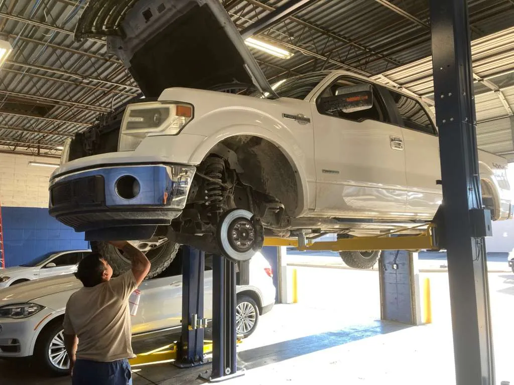 White Ford pickup truck on a hydraulic lift with the front wheel removed for brake service.