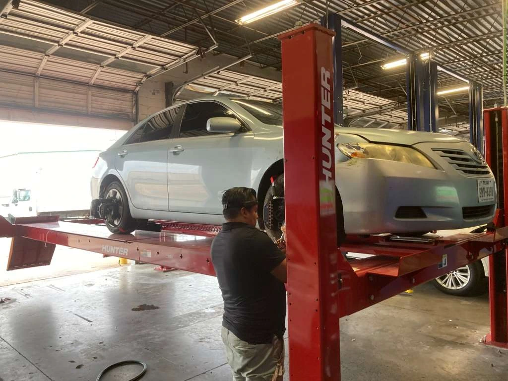 Professional technician performing wheel alignment on a sedan at an auto repair shop using a Hunter lift.