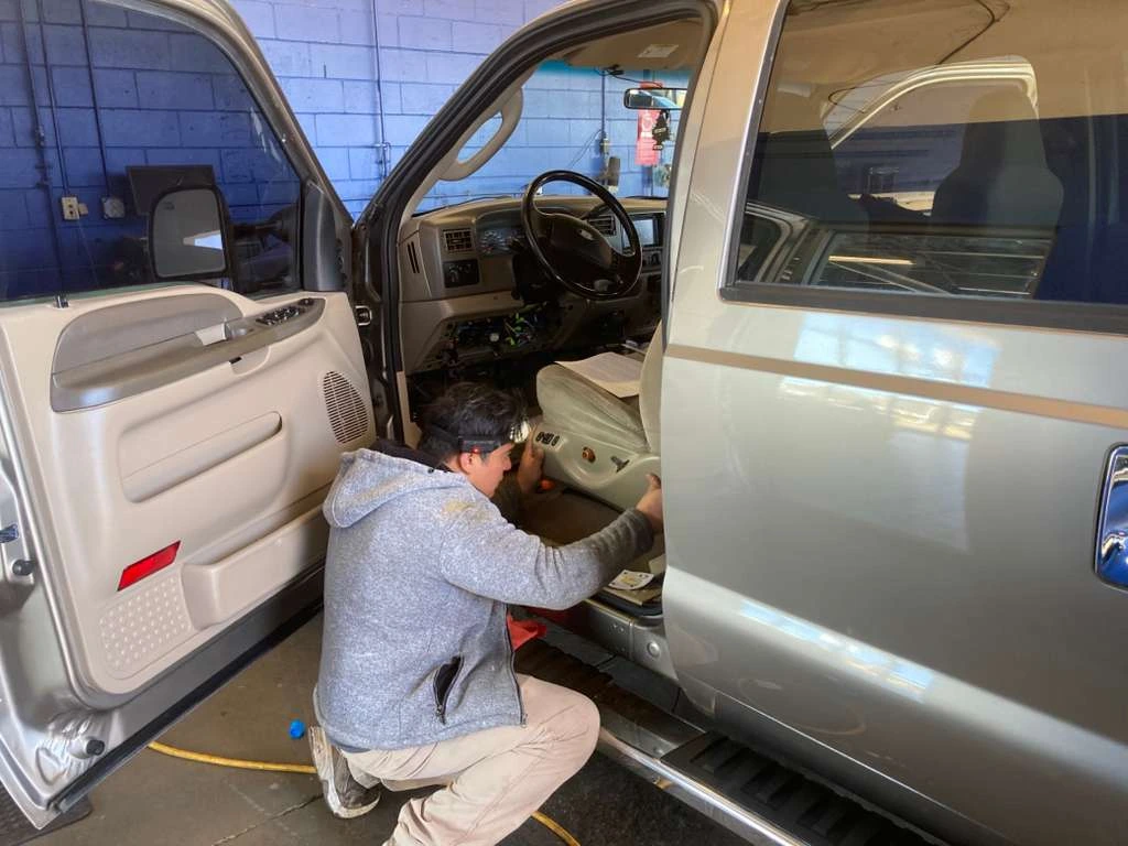 Professional technician performing interior electrical or seat repair on a vehicle at an auto repair shop
