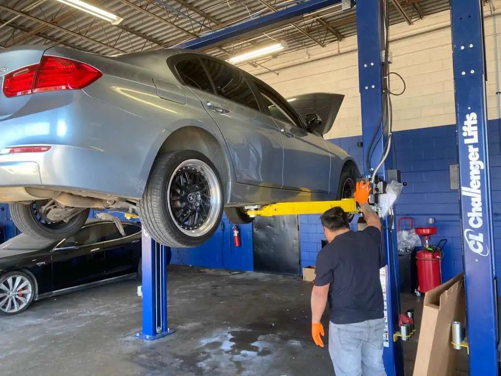 Professional mechanic performing auto repair and maintenance services on a luxury sedan using a hydraulic car lift in a modern garage.