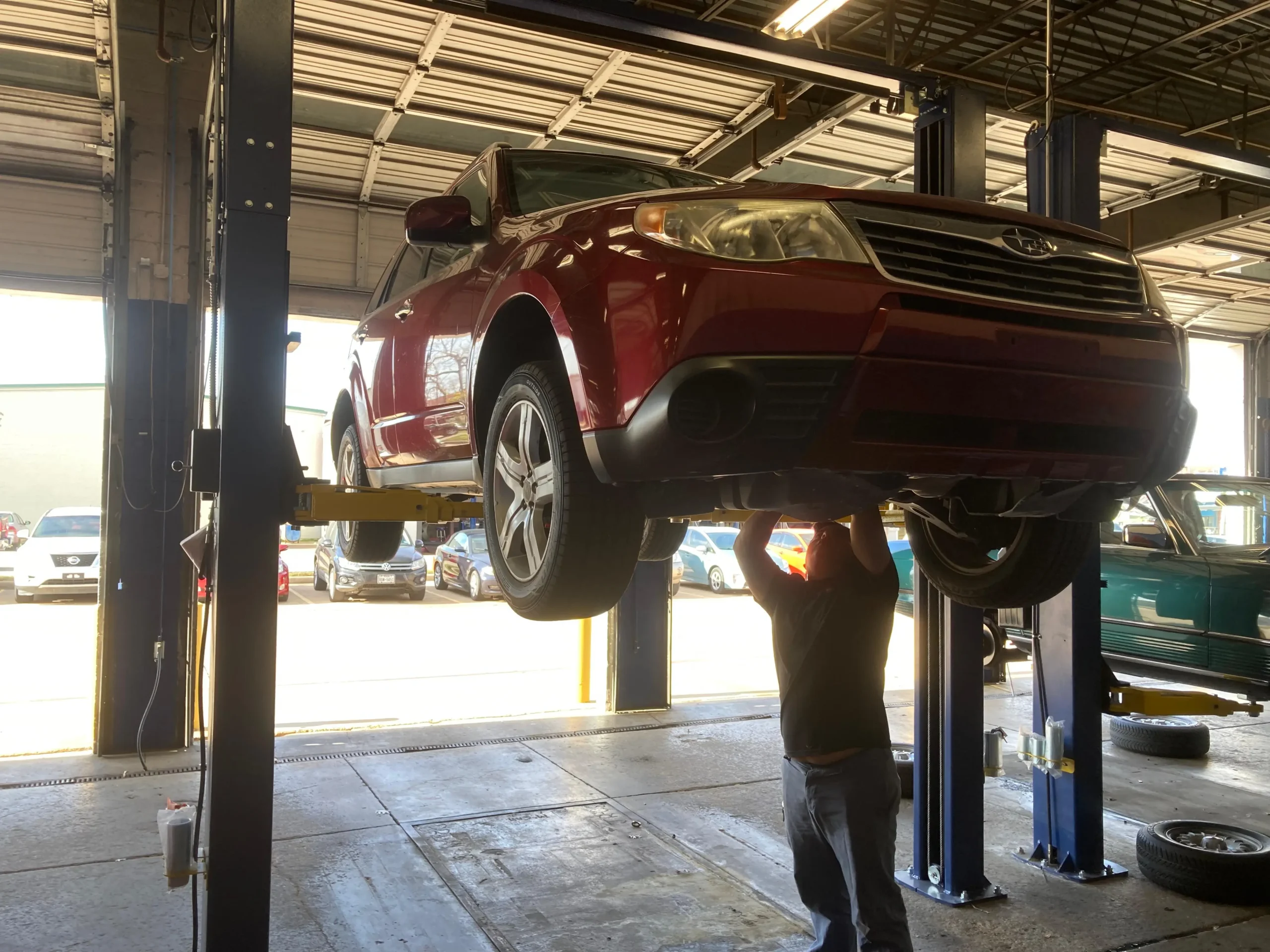 Experienced mechanic performing a detailed under-auto inspection on a red SUV in a professional garage.