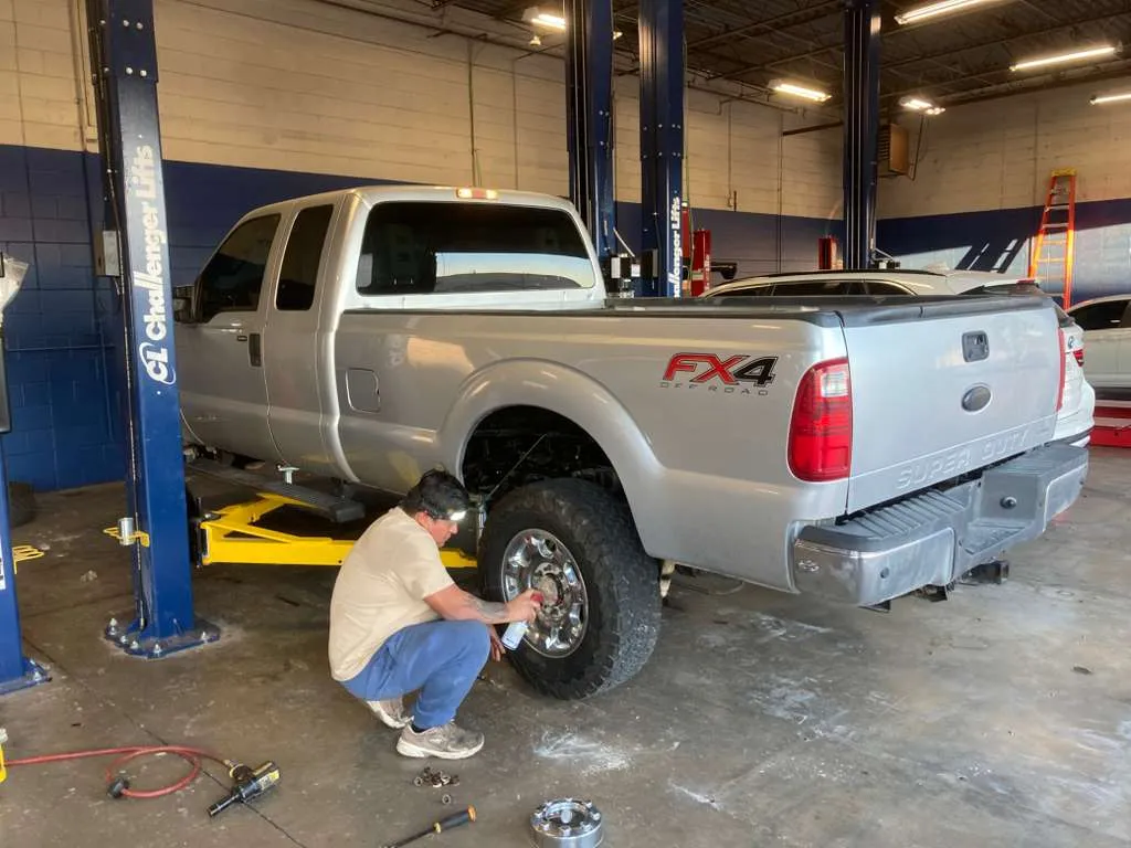 Mechanic performing tire maintenance on a silver FX4 pickup truck at Bay Area Auto.