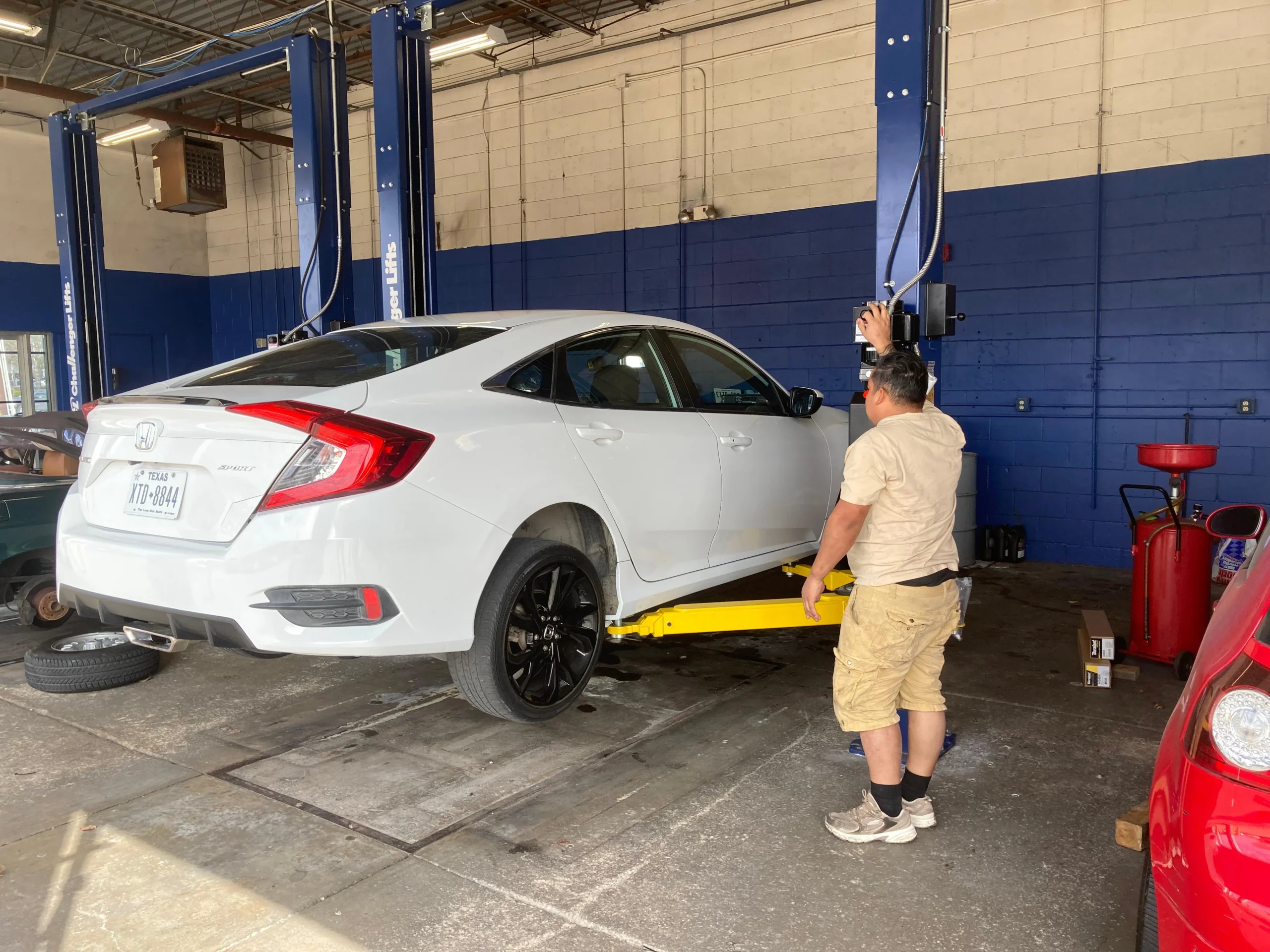 White sedan on a yellow hydraulic lift for under-car inspection at an auto repair shop